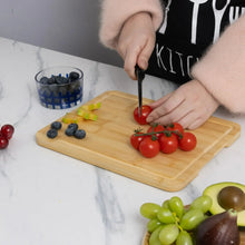 Bamboo cutting board with tomatoes and blueberries; hands slicing with a knife