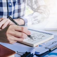Hand holding a retractable black fine-point gel pen over an open notebook