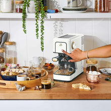 White espresso machine with cup under the spout as a hand adjusts the portafilter
