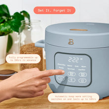 Cornflower blue electric rice cooker on countertop with lit control panel and hand.