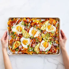 Natural aluminum baking sheet held in hands with topped nacho-style food