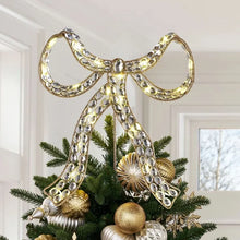 Jeweled bow tree topper with warm lights and gold-tone trim on a Christmas tree