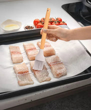 Silicone basting brush with bamboo handle brushing fish fillets on a tray