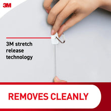 Hand pressing a white wire hook and adhesive strip onto a wall