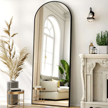 Arched full-length black-framed mirror reflecting a living room with sofa and potted plant.