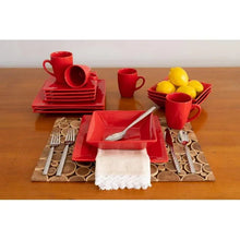Red stoneware dinner set arranged on patterned placemats with cutlery and lemons