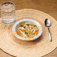 Disposable paper bowl with soup and carrots, blue-and-gold patterned rim