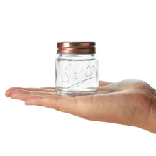 Mini mason jar shot glass with copper lid held in a hand, clear glass