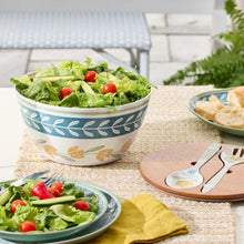 Floral salad bowl holding greens and cherry tomatoes; includes salad utensils on side.