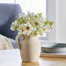 Artificial wildflower arrangement in beige ceramic jug vase with loop handle and white blooms