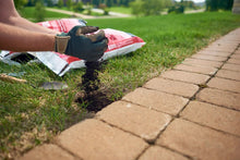 Hand spreading dark soil into lawn near walkway pavers