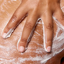 Hand applying glycolic body scrub with thick white paste on skin