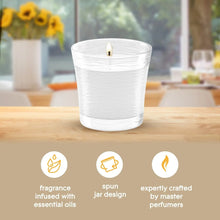 White jar candle with lit wick on wooden table, fragrance icons at the bottom