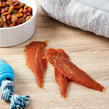 Red chicken jerky strips on a surface with a bowl of dog treats nearby