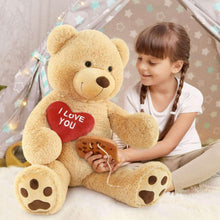 Giant teddy bear plush in light brown holding a red “I Love You” heart