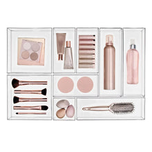 Clear 9-piece makeup drawer organizer with brushes, bottles, and face palette.