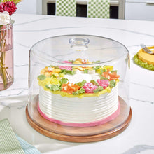 Clear dome cake plate with wood base holding a frosted layer cake