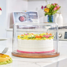 Clear dome cake plate with wood base holding a frosted cake