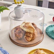 Clear dome cake plate with wood base holding assorted pastries