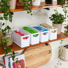 White kitchen storage bins on a shelf with green, blue, and red contents