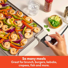 Electric griddle with shrimp and vegetables, hand adjusting the temperature probe dial