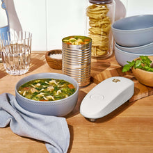 White hands-free electric can opener on a countertop beside bowls and jars