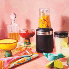 Single-serve blender with clear jar filled with yellow fruit smoothie and lid