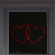 Double heart LED window silhouette with glowing red outlines in a window frame