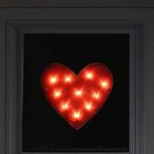 Red heart window silhouette lit from behind with glowing bulbs in a heart shape