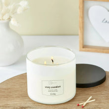 Lit Cozy Comfort scented candle in clear glass jar with black lid and centered label