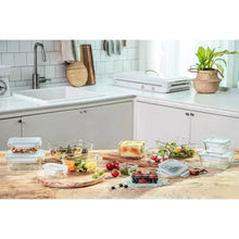 Glass food storage containers set with lids, assorted ingredients on kitchen counter.