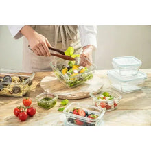 Glass food storage container being filled with salad greens, with other containers nearby.