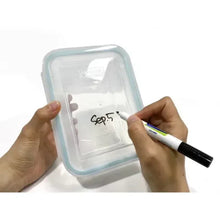 Glass food storage container with blue frame while labeling inside with a marker.