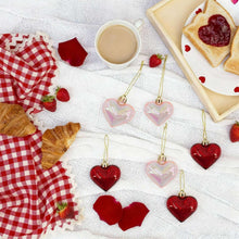 Multiple red and iridescent heart ornaments on strings with gold hanging loops
