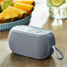 Blue small rugged Bluetooth speaker on wooden surface, fabric grille and top control icons