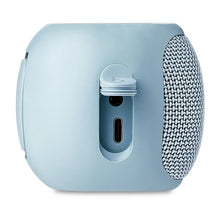 Side view of blue small rugged Bluetooth speaker with charging port panel and fabric grille