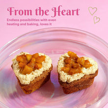 Two mini heart cakes on a clear plate beside the pink heart baking pan