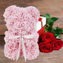 Light pink artificial rose teddy bear with white ribbon, beside red roses in box