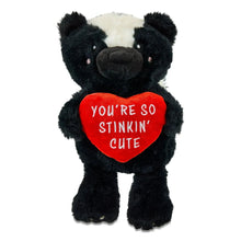 Front-facing black-and-white skunk plush holding a red heart with “YOU’RE SO STINKIN’ CUTE”