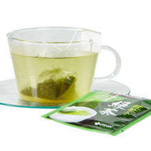 Green tea bag in a clear cup with pale green liquid and sealed tea packet