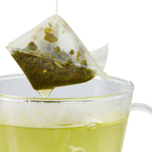 Green tea bag steeping in a clear cup with pale green infusion