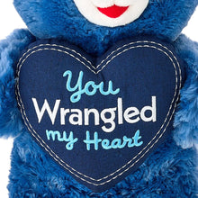 Blue teddy bear plush with navy heart patch outlined in white: “You Wrangled my Heart”