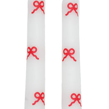 Two white taper candles with red bow pattern accents and straight sides
