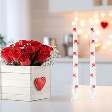 Pair of white taper candles with red bow decorations, standing upright